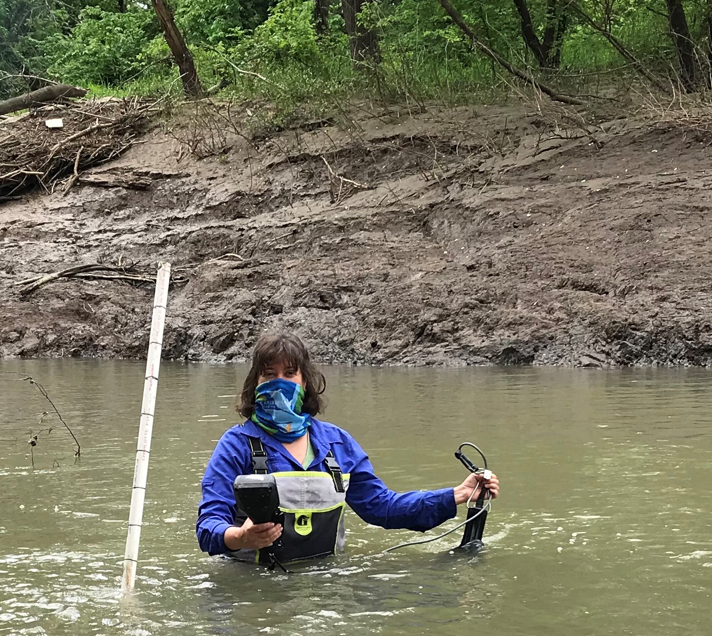 "Debbie Baker wearing waders and walking in waist-up water in river, holding research equipment"