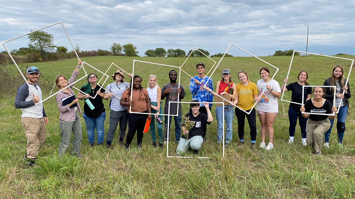 "Group of students standing in field and holding plant survey quadrat frames as if they are picture frames"