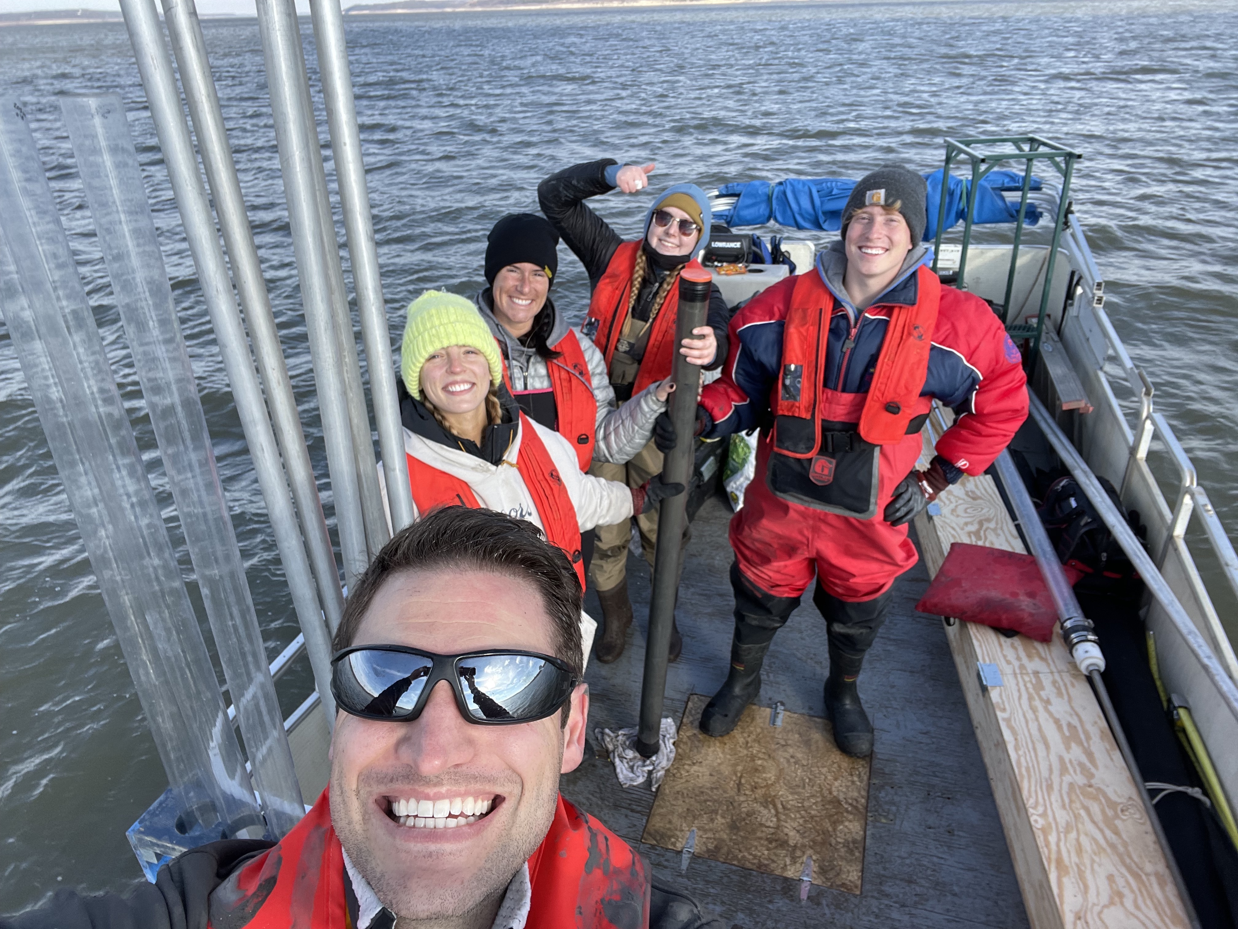"Researcher and group of students standing on boat in lake and smiling at camera"