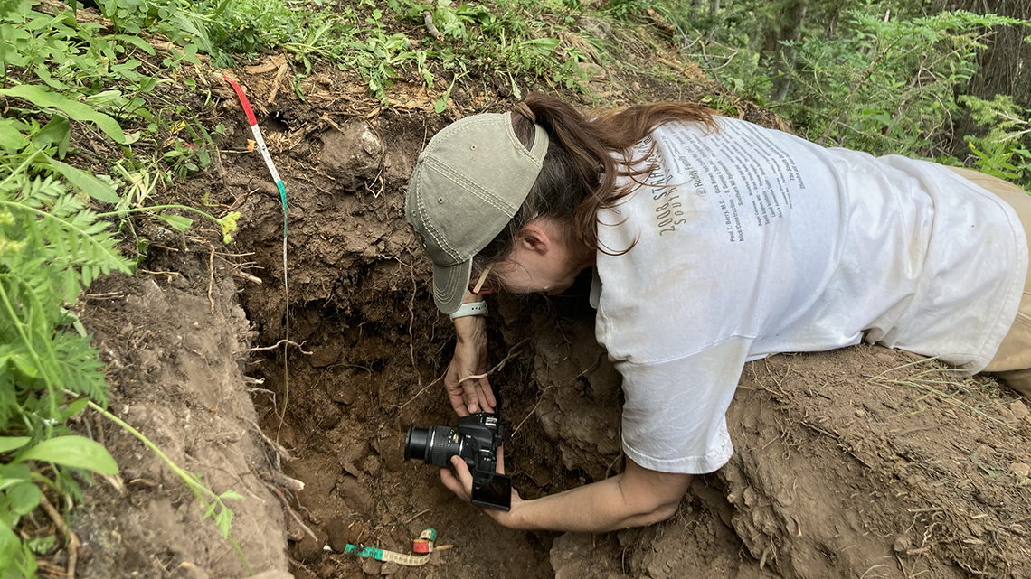 &quot;Researcher lying on ground over soil pit holding camera&quot;